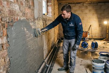 A specialist contractor applying waterproofing membrane to a basement retaining wall during a residential basement waterproofing project in the UK