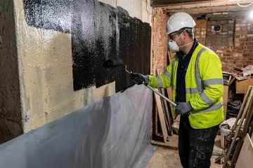 Contractor applying waterproofing membrane to basement wall in UK construction project